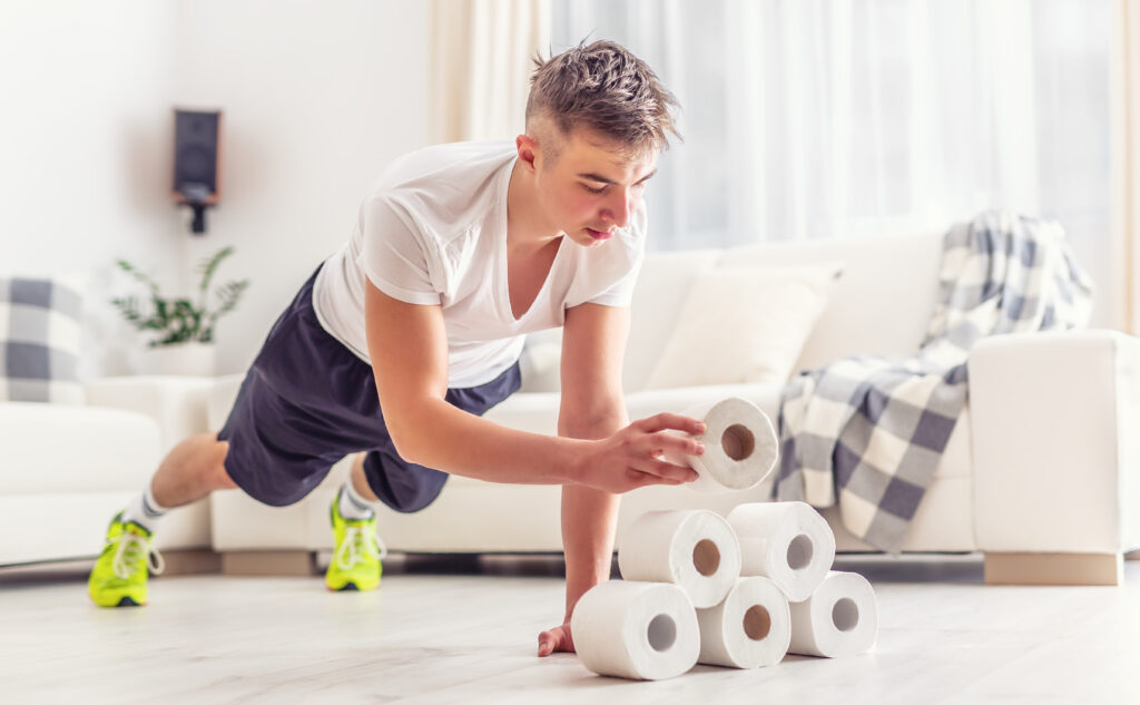 A bored and athletic young man is using toilet paper as support for his plank.